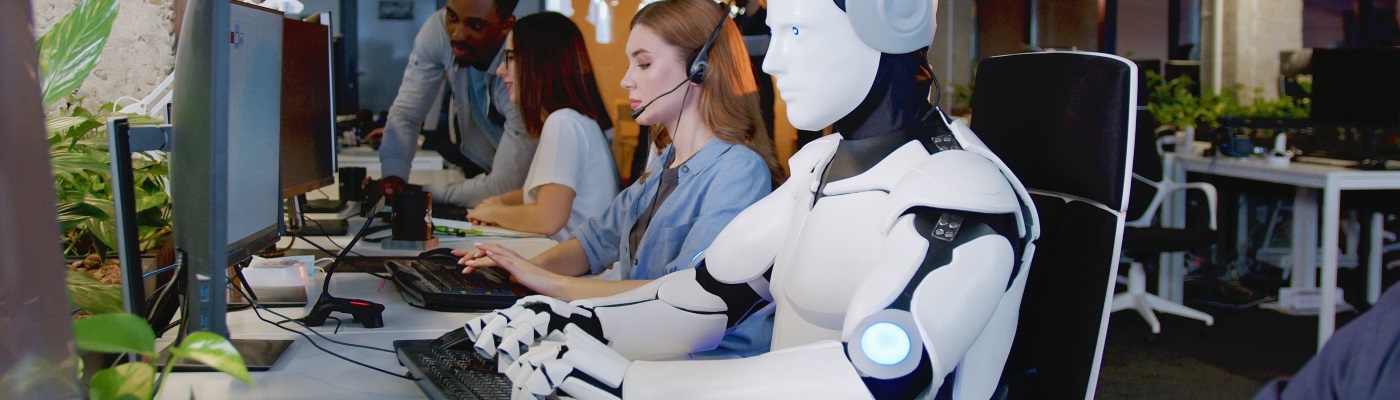 Robot sat amongst humans working on computers 