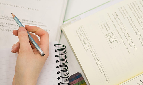 Close up of student's hand, pencil and book