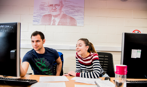 Two students smiling while looking at a computer screen