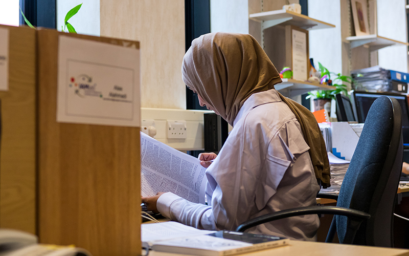 A student looking at papers in front of her computer screen